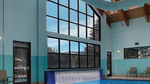 A large indoor swimming pool with clear blue water, a wooden ceiling, and large windows offering views of the outdoors.