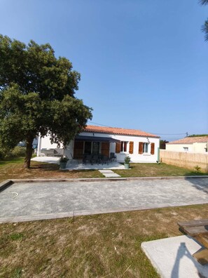 Ein zweistöckiges Haus mit Ziegeldach, einer Terrasse mit Gartenmöbeln und einem großen Baum im Hof.