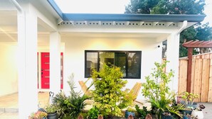 Una casa con porche cubierto, puerta roja y varias macetas con plantas.