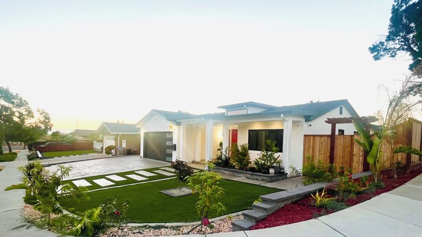 Una casa moderna de dos pisos con un jardín bien cuidado, un patio y una valla de madera.
