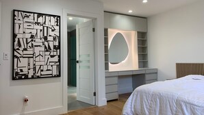 Un dormitorio moderno con una cama grande, un armario empotrado, un espejo y una obra de arte abstracta en la pared.