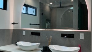 Un baño moderno con tragaluz, dos lavamanos grandes blancos y un espejo amplio.
