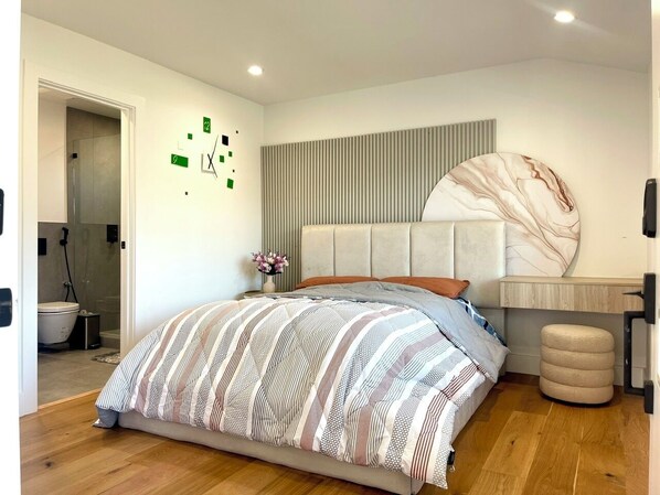 A modern bedroom with a large bed, a headboard, a bedside table with a vase of flowers, and a wall-mounted clock.