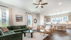 A modern living room with a green sofa, a coffee table, and a dining area with a kitchen in the background. - UNCC 4BR | Pet-Friendly Stay (Charlotte)