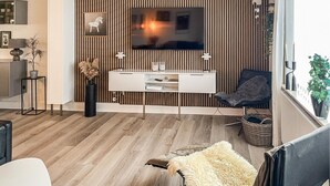 A modern living room with a TV, white console, and a dark armchair.