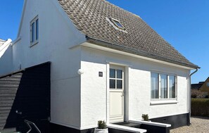 Una casa blanca con techo gris, puerta principal y una ventana pequeña.