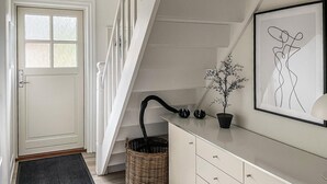A modern interior with a white door, a staircase, a wall-mounted plant, and a framed artwork.