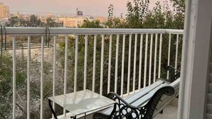 Un balcon avec une balustrade en métal, une table blanche et un banc noir.