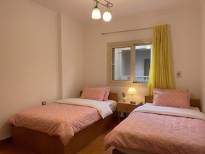 Une chambre avec deux lits, une fenĂȘtre avec des rideaux, une table de chevet avec une lampe et un luminaire au plafond.