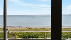 A view of the sea through a window, with a sandy beach and a grassy area in the foreground. - Amazing home in Otterup with WiFi (Otterup)