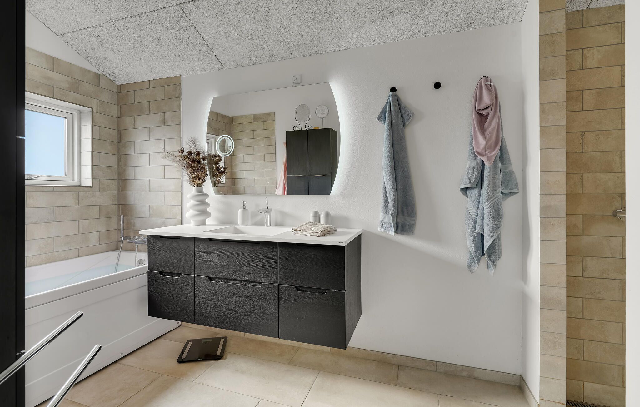Une salle de bain moderne avec un meuble-lavabo blanc, des armoires sombres, un miroir et des serviettes accrochées au mur.