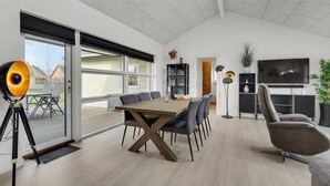 A modern living room with a dining area, large windows, and a flat-screen TV.