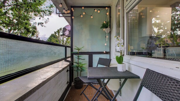 A balcony with a table and chairs, a potted plant, and a string of lights.