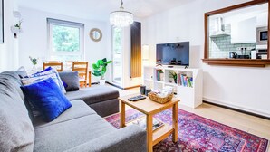 A modern living room with a grey sofa, a wooden coffee table, a TV, and a bookshelf.