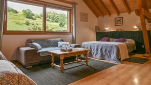 Una habitación acogedora con techo de madera, un sofá, una cama, una mesa con vasos y vistas a un paisaje verde.