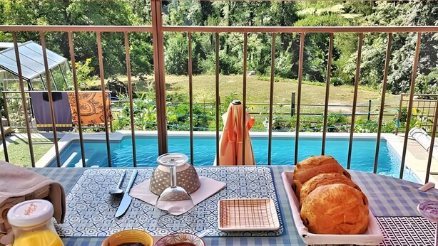 Una mesa con alimentos para el desayuno, una botella de jugo y vistas a una piscina y al paisaje.