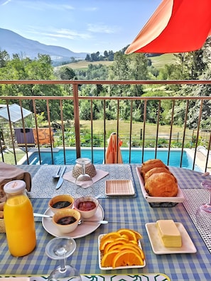 A table with breakfast items, a bottle of juice, and a view of a swimming pool and landscape.