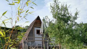 Ein rustikales Holzhaus mit Satteldach, umgeben von einem Garten mit Teich und verschiedenen Pflanzen.