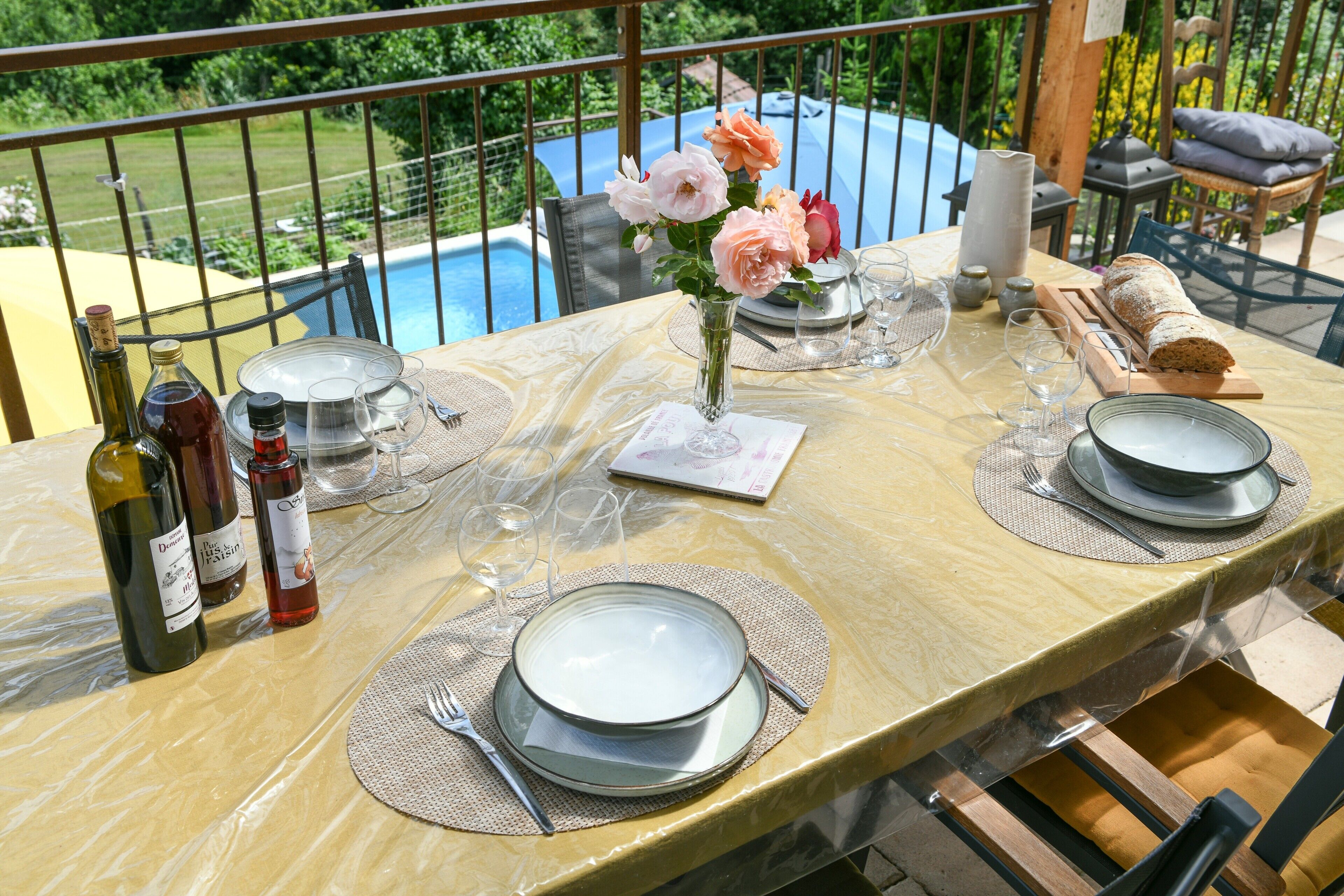A table set for dining with plates, cutlery, and a loaf of bread, overlooking a swimming pool.
