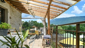 Eine überdachte Terrasse im Freien mit Tisch und Stühlen, einem Blumentopf und Blick auf eine Berglandschaft.