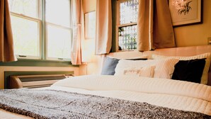 Un dormitorio con cama, ventana con cortinas, radiador y aire acondicionado de pared.