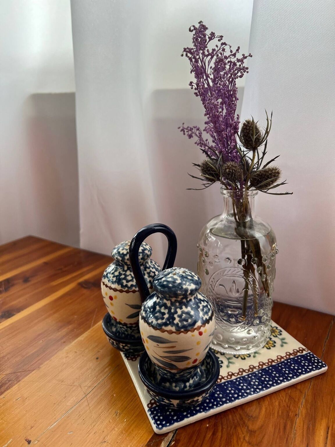 A wooden table with a ceramic tea set and a vase with dried flowers.