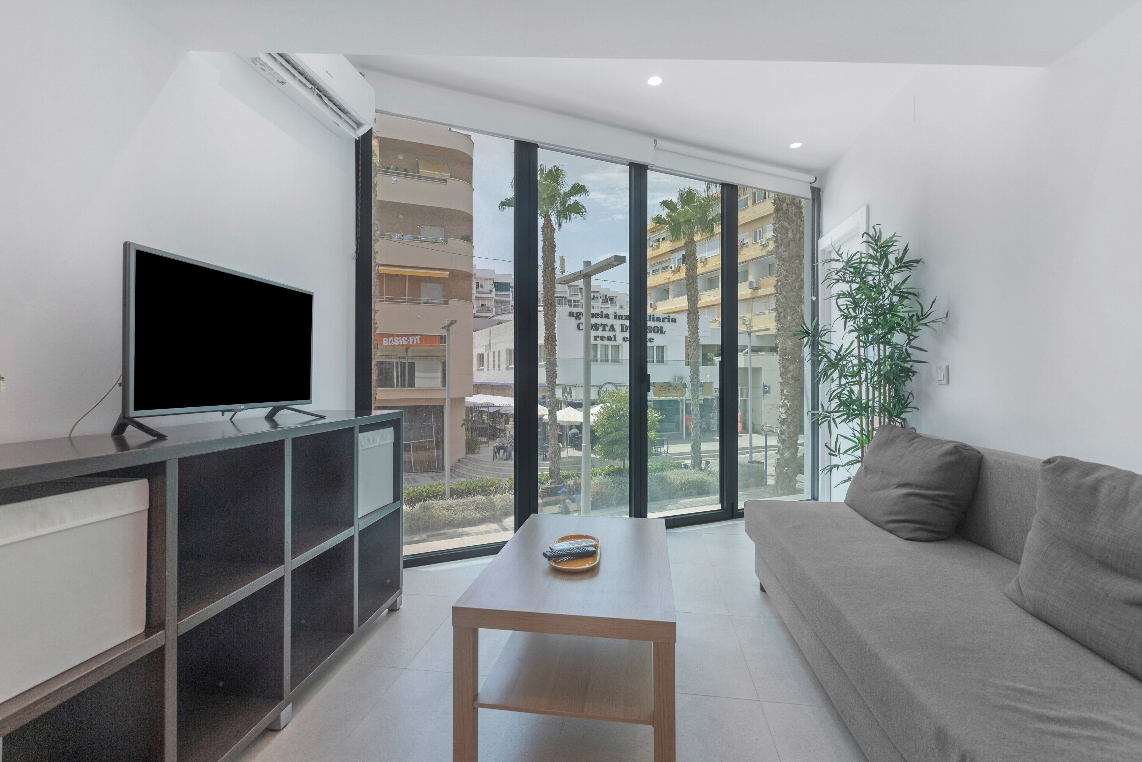 Una sala de estar moderna con un televisor de pantalla plana, una mesa de madera, un sofá y ventanas amplias que ofrecen vistas de la ciudad.