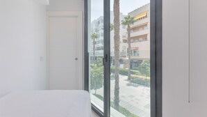 A bedroom with a large window, a bed, and a view of a building and palm trees outside. - Apartment 'Room 3' with Wi-Fi and Air Conditioning (Torremolinos)
