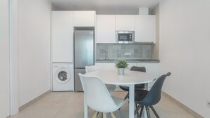 A compact kitchen with a refrigerator, microwave, and washing machine, a round dining table with chairs, and a potted plant. - Apartment 'Room 3' with Wi-Fi and Air Conditioning (Torremolinos)