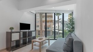 A modern living room with a flat-screen TV, a grey sofa, a wooden coffee table, and a glass door leading to an outdoor area with palm trees. - Apartment 'Room 3' with Wi-Fi and Air Conditioning (Torremolinos)