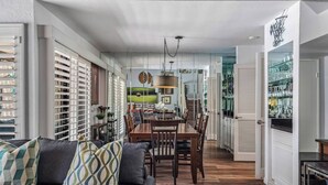A spacious living area with a sofa, dining table, and chairs, leading to a kitchen with a glass door.