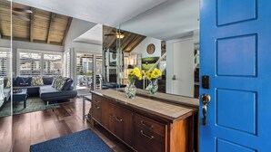 A modern living room with a blue door, wooden ceiling, and a large mirror reflecting the room.