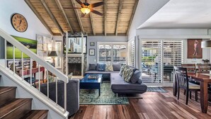 A spacious living room with a wooden ceiling, a large sofa, a dining area with a table and chairs, and a staircase leading to another level.