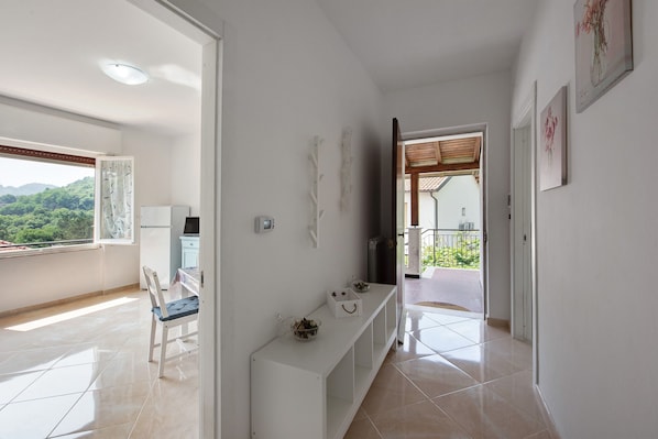 A hallway with a white console table, a chair, and a view of a balcony with a green landscape.