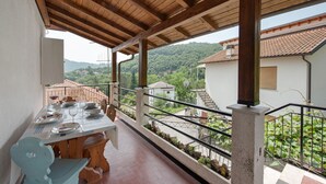 A balcony with a wooden ceiling, a dining table set with plates and glasses, and a view of a hillside with buildings. - Villa 'Chiara' with Mountain View and Private Terrace (Lumarzo)