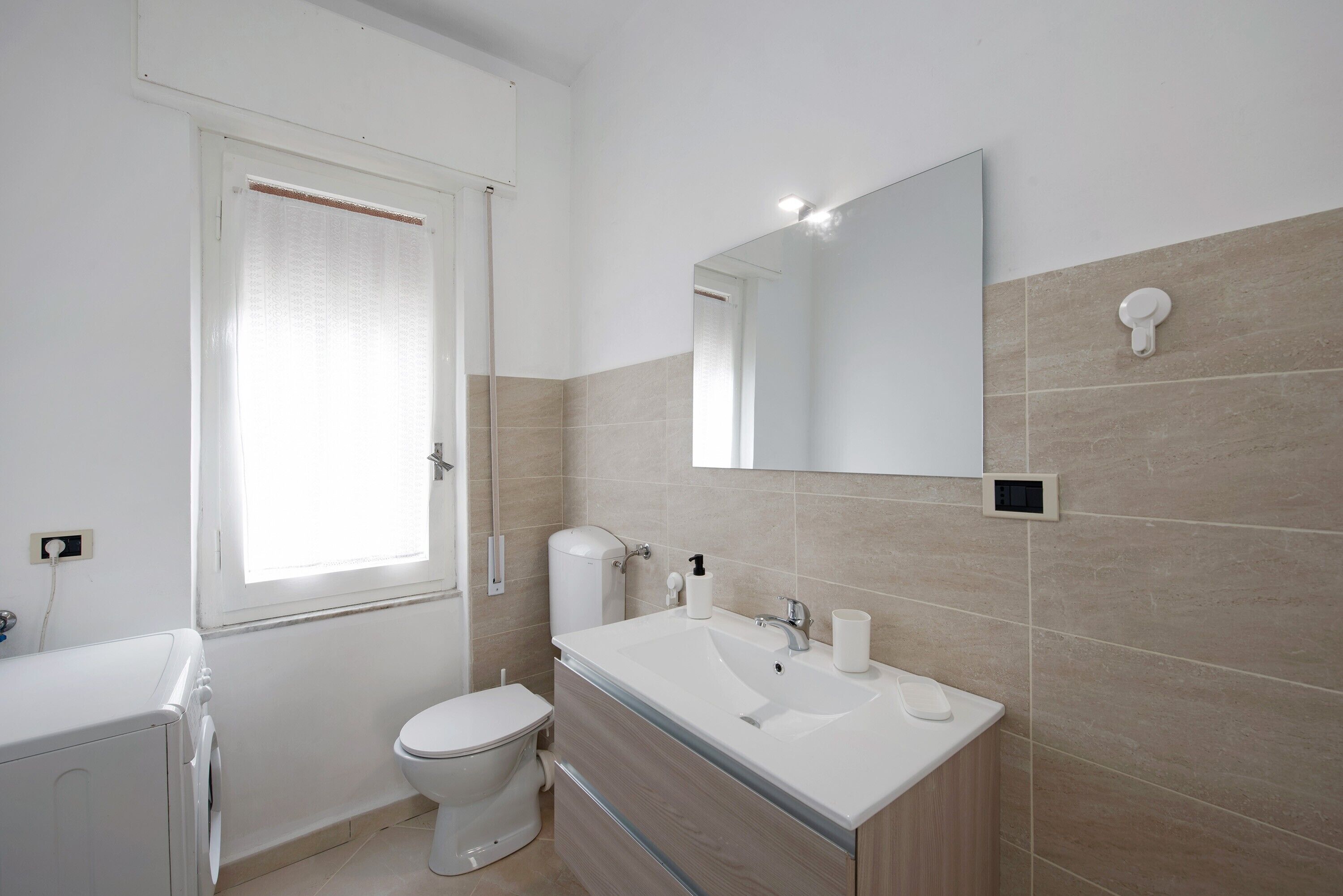 A bathroom with a toilet, sink, mirror, and window.