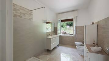 Een moderne badkamer met douche, toilet en wastafel, met een grote spiegel en uitzicht op het buitengebied.