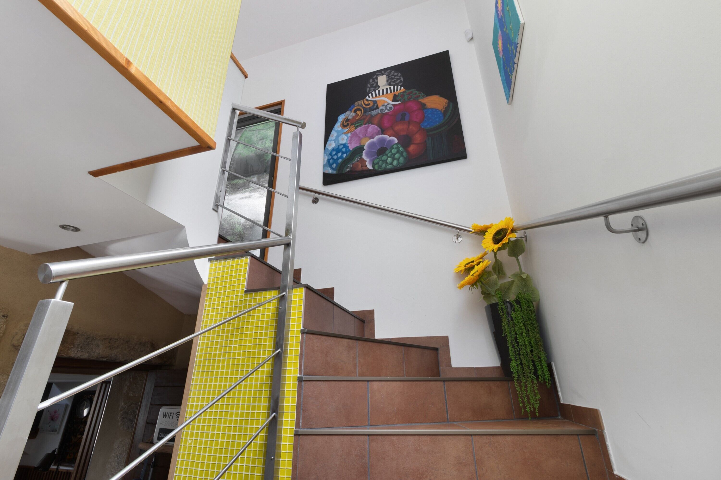A staircase with a metal handrail, a yellow tiled wall, and a painting of fruits on the wall.