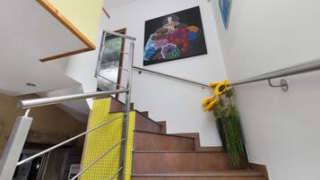 A staircase with a metal handrail, a yellow tiled wall, and a painting of fruits on the wall.