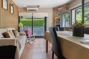 A room with a bed, a dining table with chairs, a window with a view of greenery, and an air conditioning unit. - Holiday Home 'Cevidade' with Lake View, Wi-Fi and Air Conditioning (Melgaço)