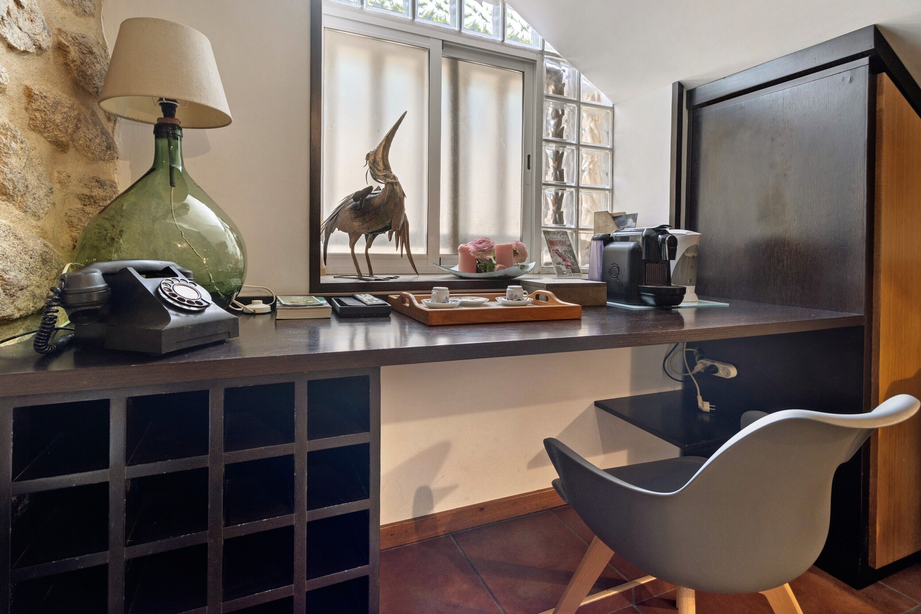 A kitchen with a green lamp, a telephone, a decorative bird, a coffee maker, and a window with a view.