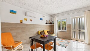 Un comedor con una mesa, sillas y un sofá. Hay una ventana con cortinas, una puerta y un aire acondicionado instalado en la pared.