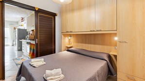 Un dormitorio con cama, armario de madera, mesita de noche y vistas a la cocina.