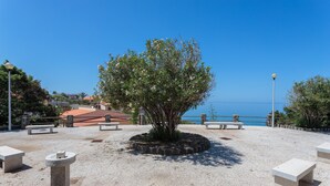 Un espacio exterior empedrado con un árbol central, bancos y una vista despejada del mar.