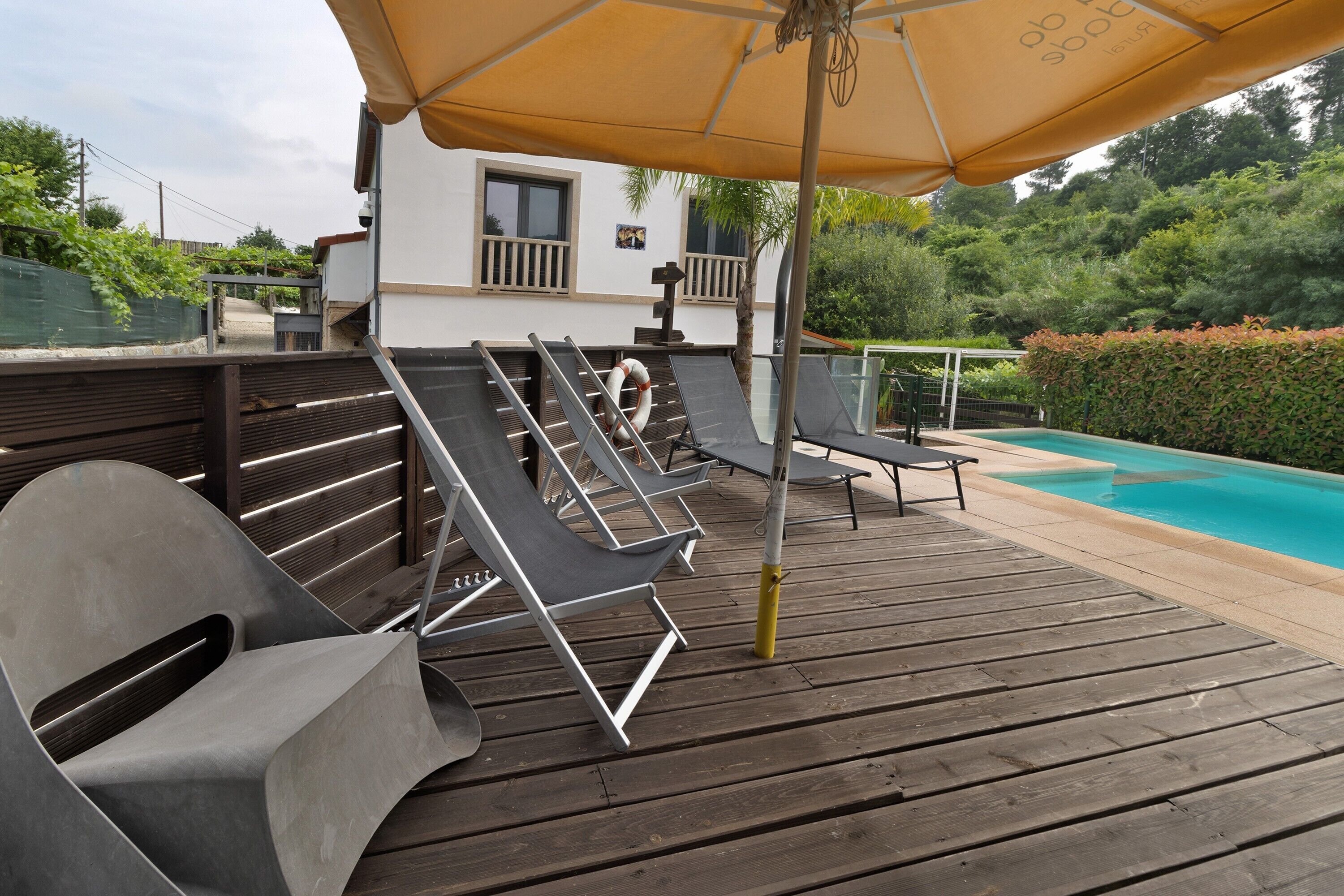 Eine Holzterrasse mit Liegestühlen, einem Pool und einem Gebäude mit weißer Fassade.