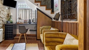Un espace de vie comprenant un canapé, une table basse, un téléviseur fixé à un mur en pierre, un escalier avec des marches en bois et un coin cuisine avec un comptoir et une chaise.