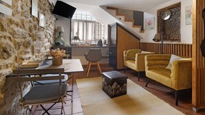 Un salon chaleureux avec un mur en pierre, un coin repas avec une table et des chaises, un canapé et un escalier.