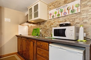 A kitchen with a microwave, a green food processor, wooden cabinets, and a wall-mounted sign about herbs and spices.