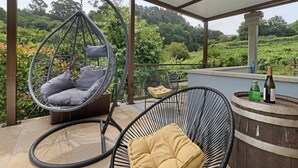 Un espace extérieur abrité, aménagé avec des sièges, comprenant un fauteuil suspendu, un fauteuil rembourré et un tonneau en bois contenant des bouteilles.