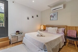 A bedroom with a bed, bedside table, nightstand, and a window.
